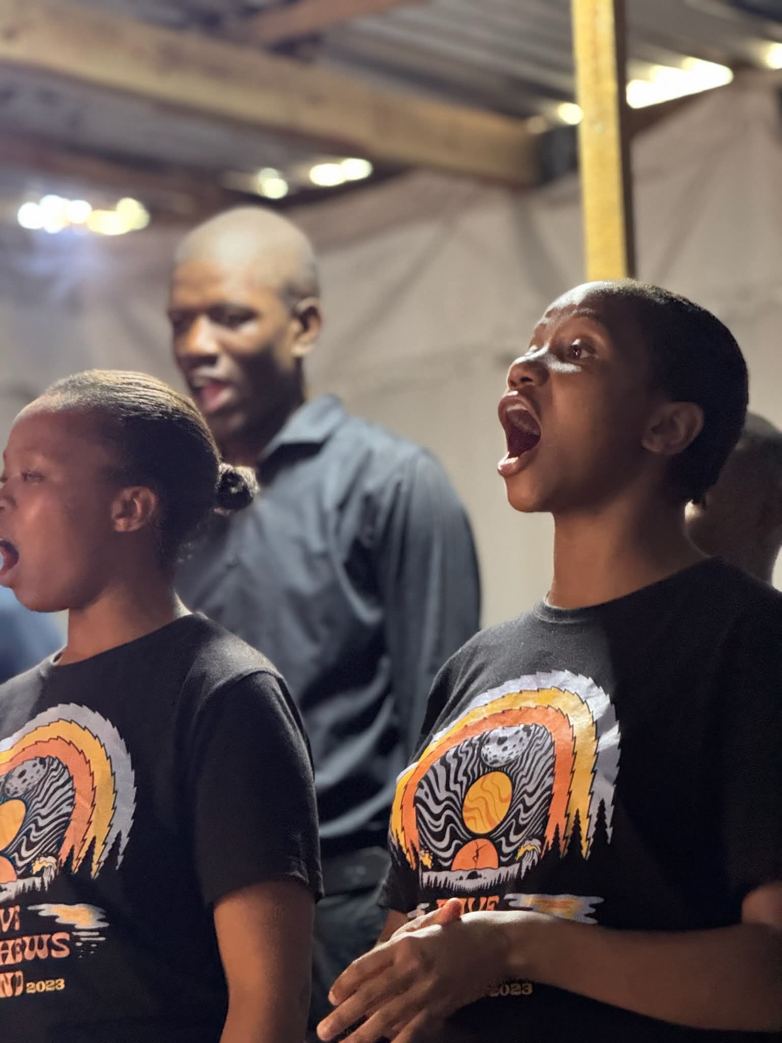 Thanda Choir members singing, wearing Dave Matthews Band 2023 tour shirts.